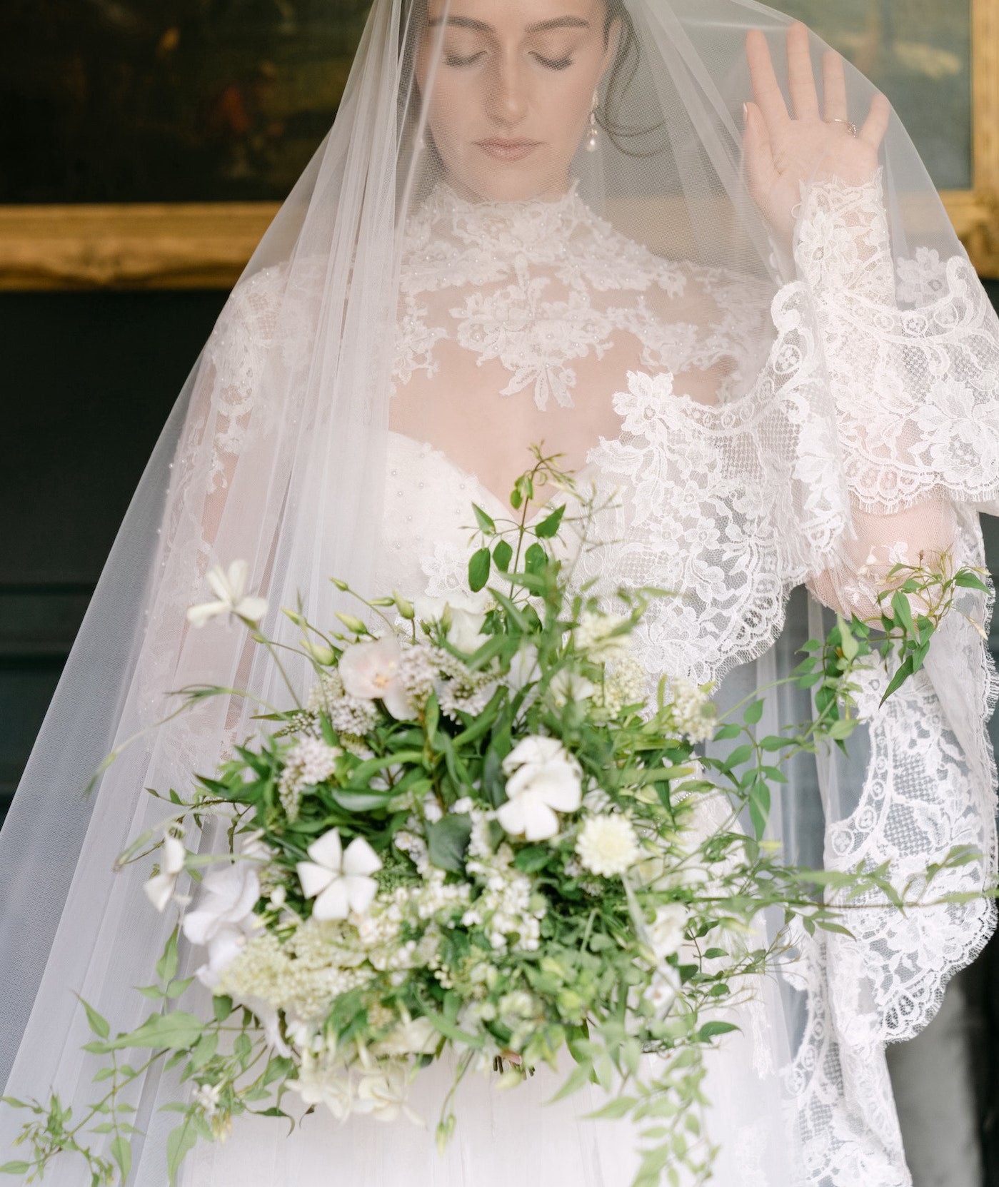 Bride holding a bouquet of flowers with a cusom veil and intircate lace sleeves.