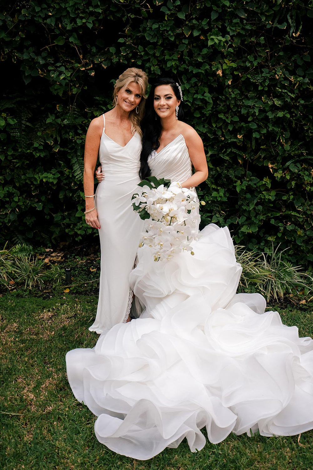 outdoor portrait of bride in the Chelsea wedding dress by Angela Kim Couture, showing the slim satin mermaid skirt contrasted against the dramatic cascading organza ruffle cathedral train, paired with a white orchid cascade bouquet
