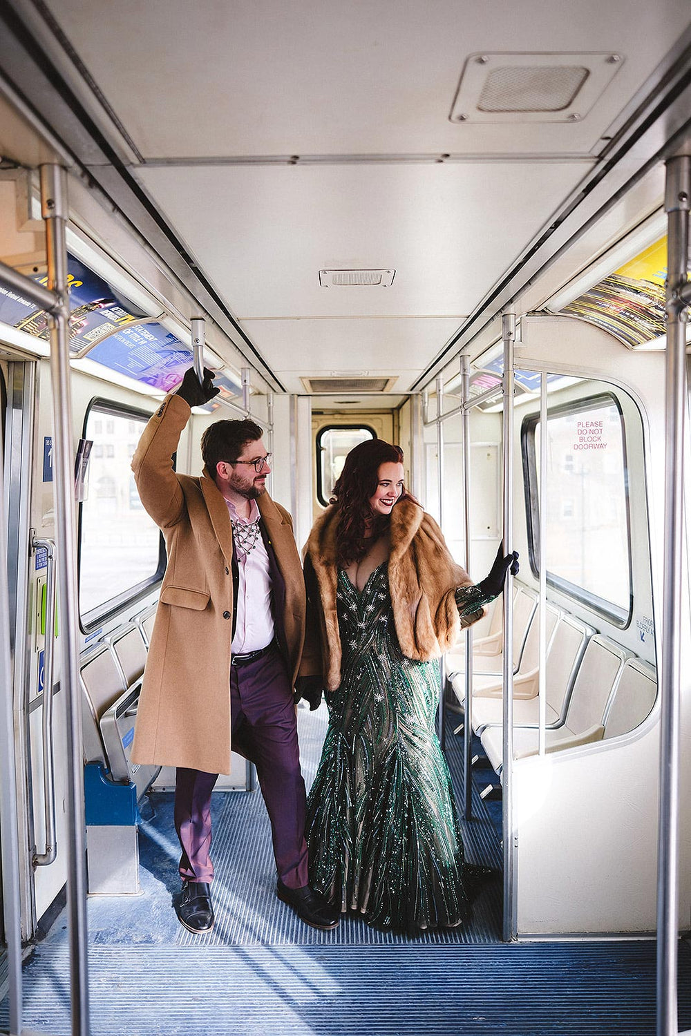 Bride and groom posing playfully inside a city trolley or subway car, bride wearing the Jessica forest green beaded wedding gown by Angela Kim Couture with a vintage fur cape and black gloves for a glamorous winter wedding look