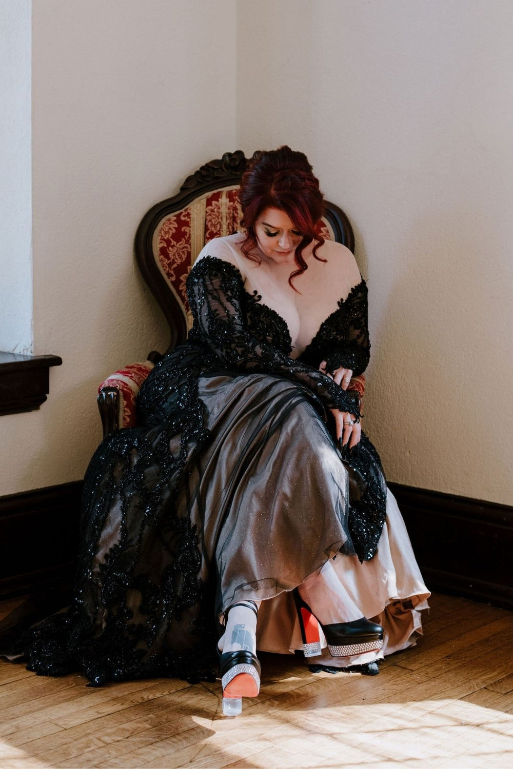 Bride seated in a vintage armchair  — black lace fit-and-flare skirt with nude underlining, black crystal-embellished red-sole platform heels (Louboutin), Kati gothic gown by Angela Kim Couture
