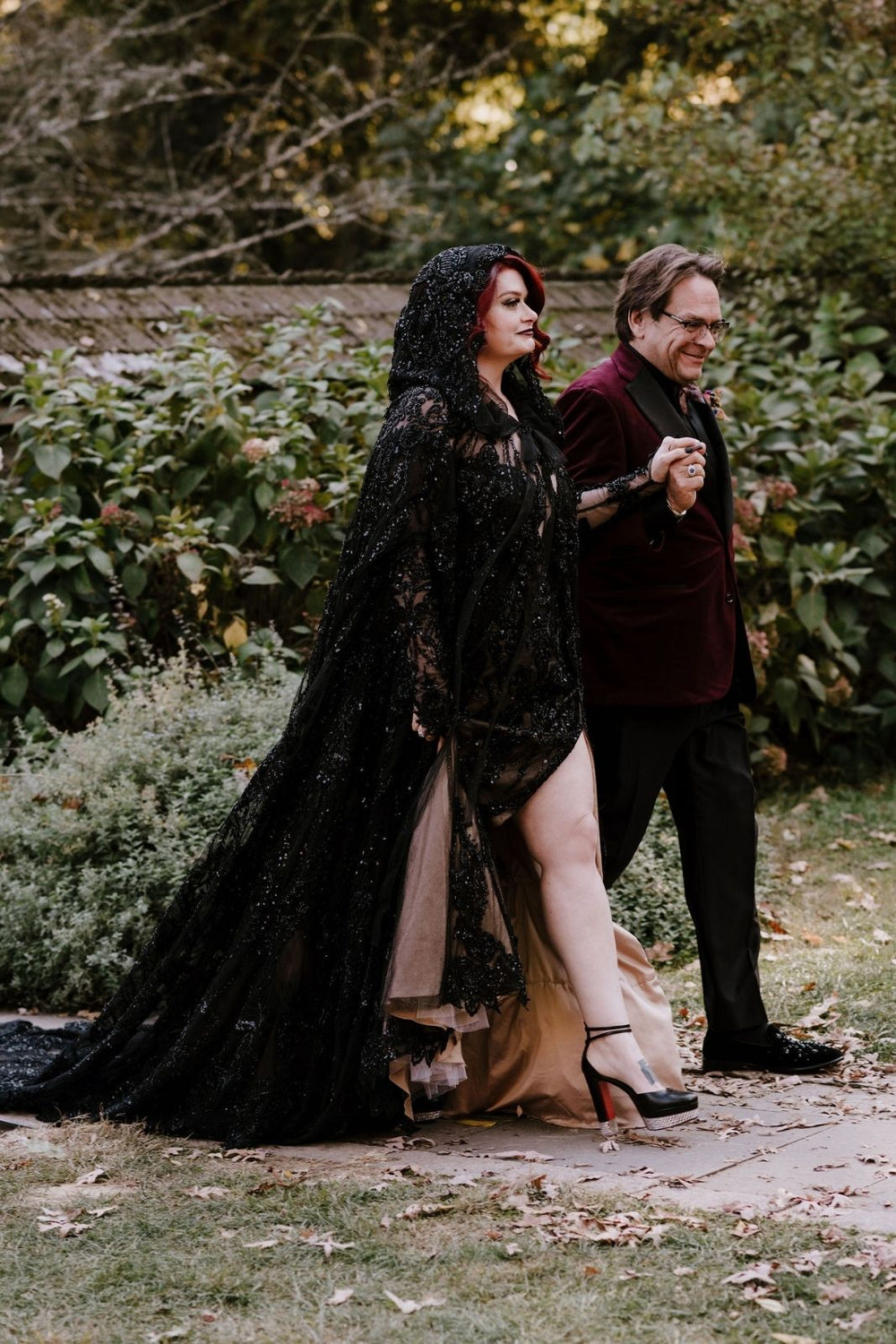 Kati black lace wedding gown by Angela Kim Couture with thigh-high slit open, black lace train on ground, and a matching cape