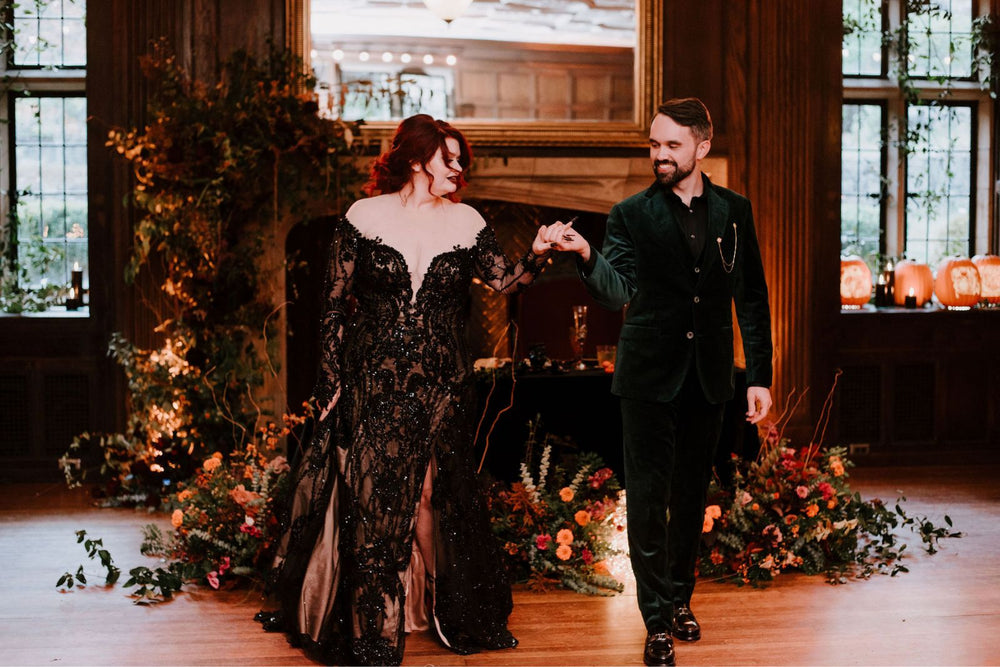 Bride and groom full-length portrait in a gothic wedding reception hall — bride in the Kati black lace beaded wedding gown by Angela Kim Couture with deep plunging neckline and fit-and-flare slit skirt