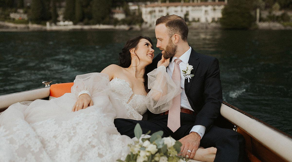 Bride and groom couple portrait by an Italian lake wearing the Morgan couture wedding dress by Angela Kim Couture with sheer bishop sleeves and lace bodice