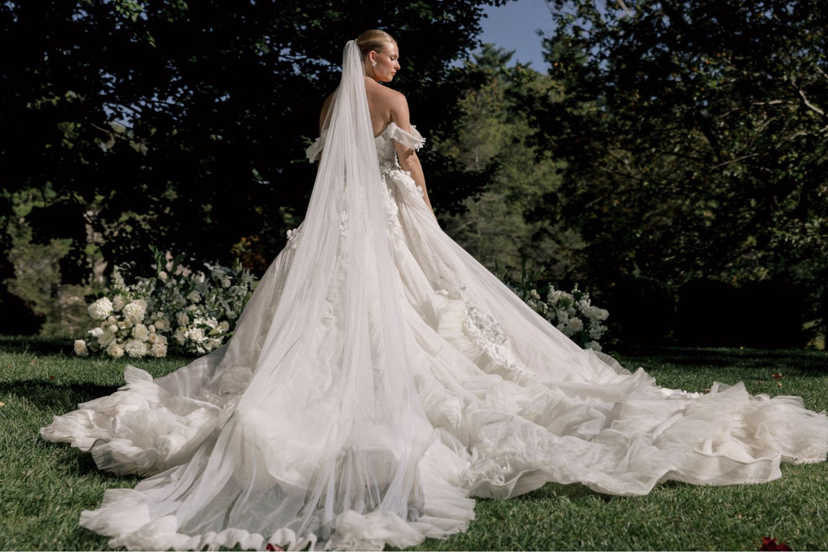 Woman in a breathtaking white wedding dress with a long train standing outdoors.