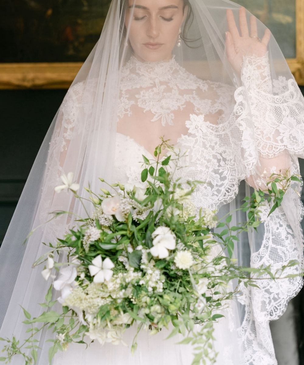 Close-up detail of Blaire's custom lace wedding gown by Angela Kim Couture featuring delicate lace trim alongside a lush white and green garden bridal bouquet