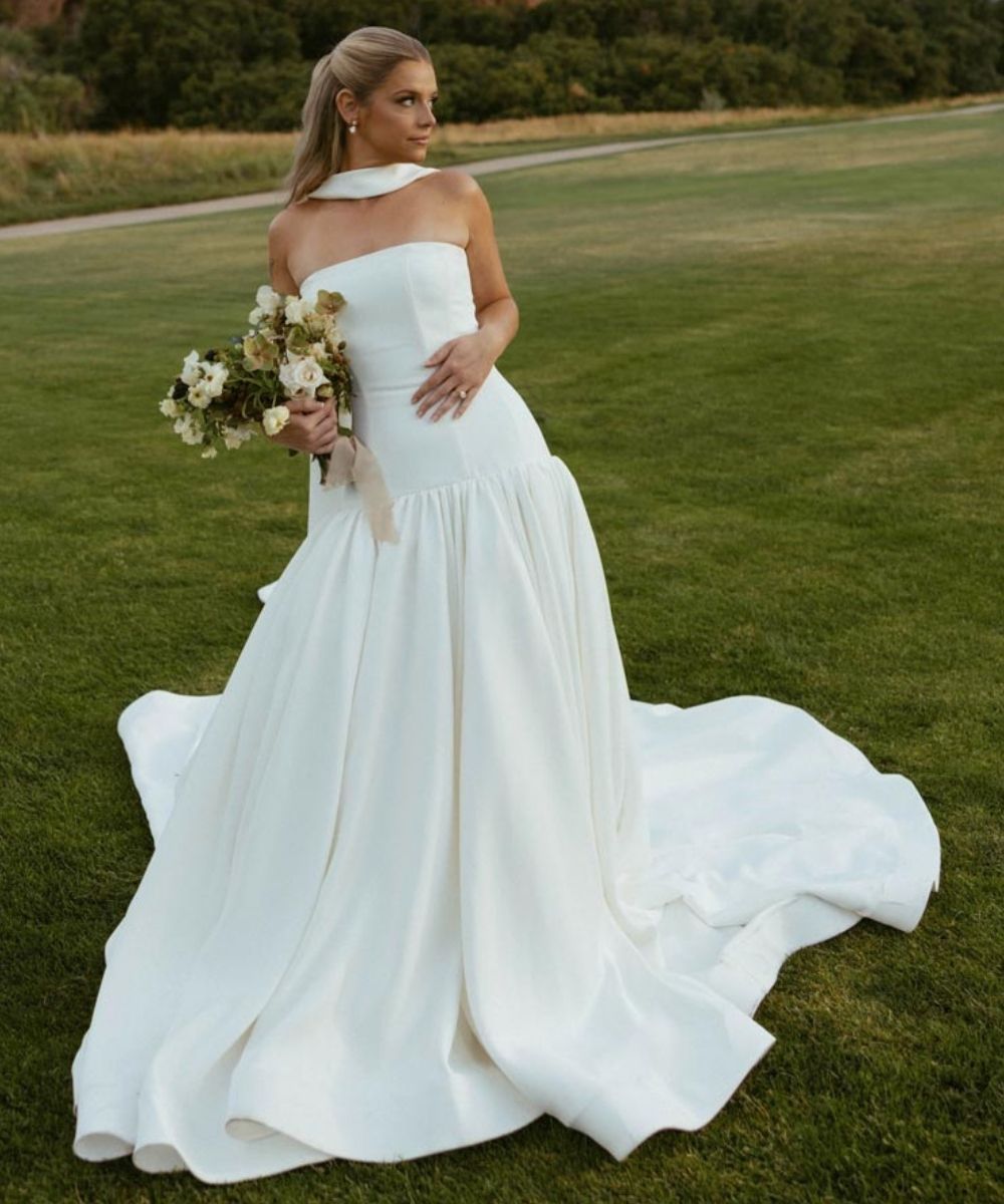 Bride in a custom minimalist strapless white wedding dress with a dramatic draped silk neck veil and full flowing cathedral train photographed outdoors at golden hour