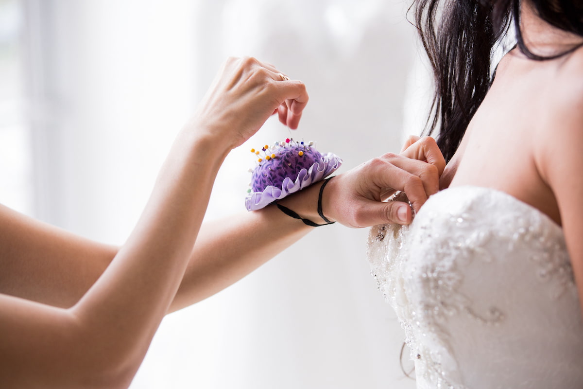 Angela Kim Couture designer carefully pinning and fitting a custom wedding dress on a bride during a bespoke bridal fitting appointment showcasing the hands-on couture design process