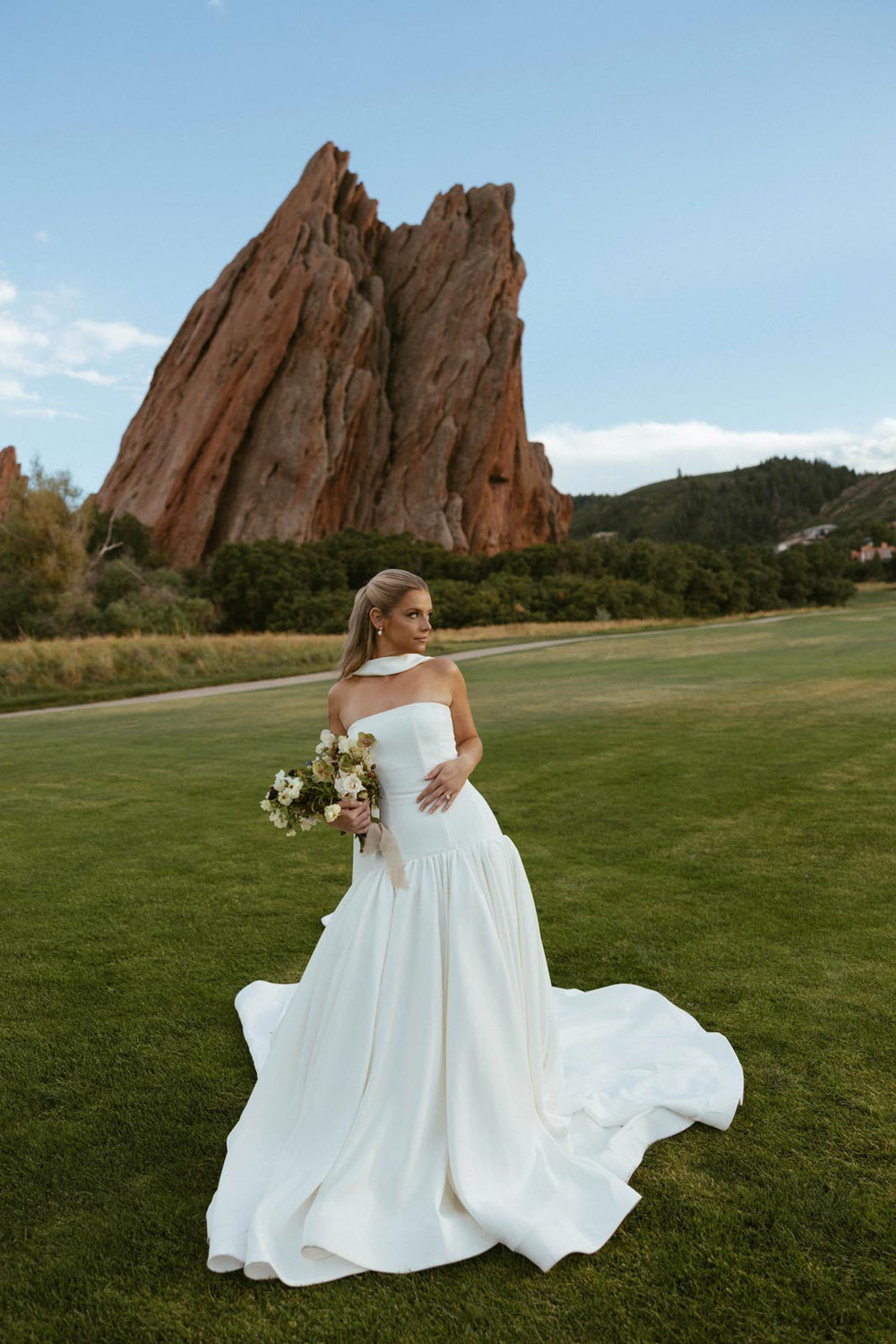 Full-length portrait of bride Hannah in her custom Angela Kim Couture strapless crepe wedding dress with silk neck veil, photographed against the dramatic red sandstone formations of Red Rocks Colorado