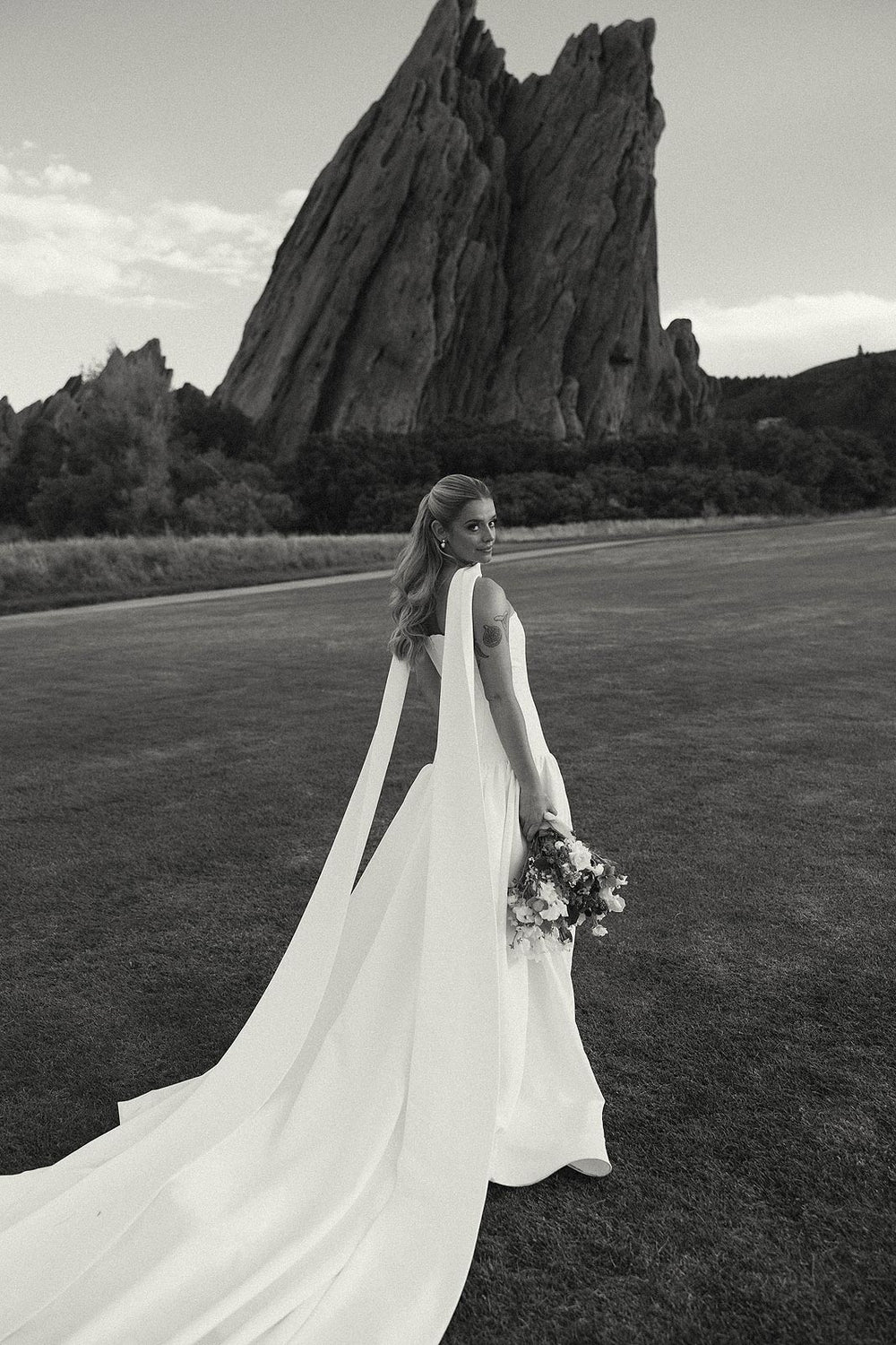 Black and white aerial close-up of Hannah's custom heavy-weight crepe wedding gown skirt and horsehair hem by Angela Kim Couture, showing the clean structured volume of the A-line silhouette on grass