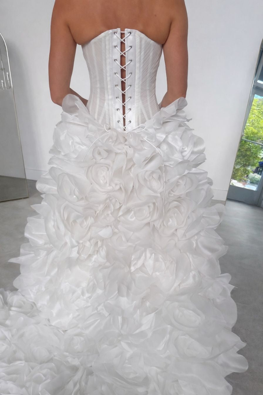 Back view of strapless white wedding gown with lace-up corset bodice and layered ruffle rose skirt during bridal fitting