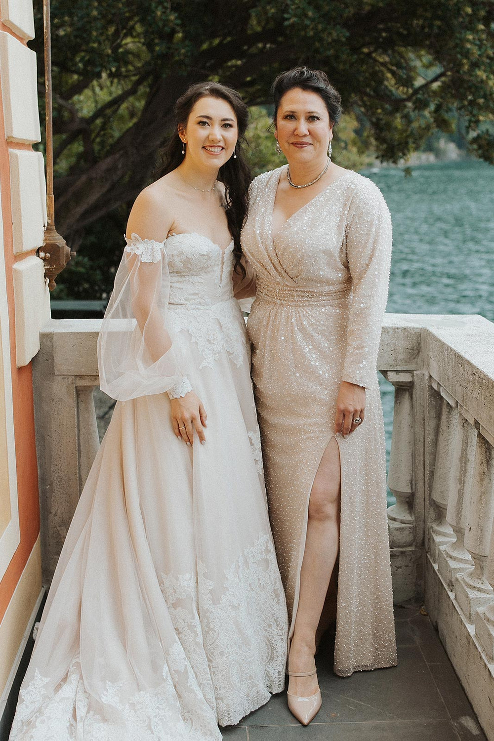 bride in the Morgan lace wedding dress by Angela Kim Couture standing beside the mother of the bride in a champagne beaded gown at the Italian wedding venue.