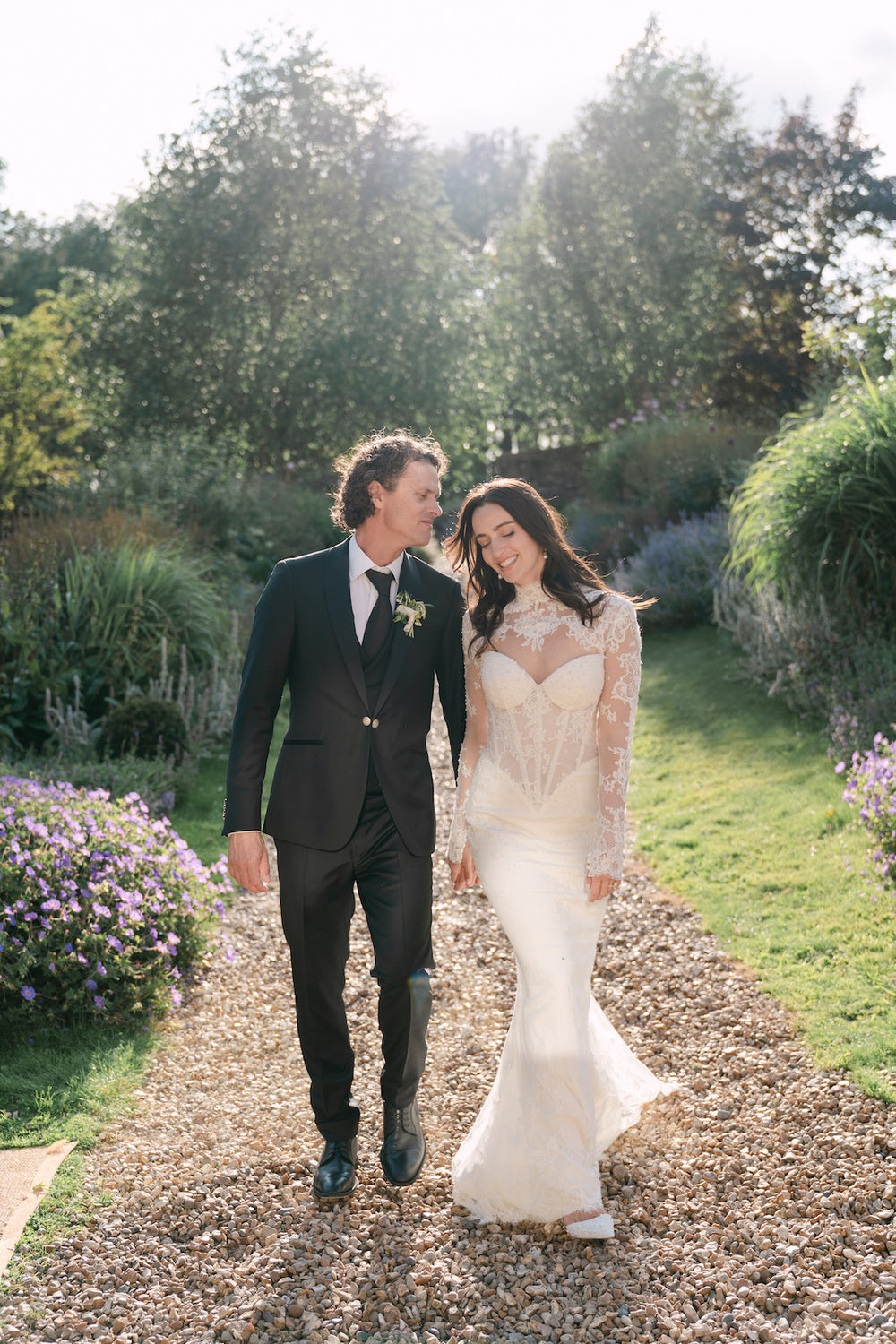 Romantic portrait of Blaire and her groom walking hand-in-hand under a lush green tree canopy, revealing the fit-and-flare silhouette of her custom Angela Kim Couture wedding gown