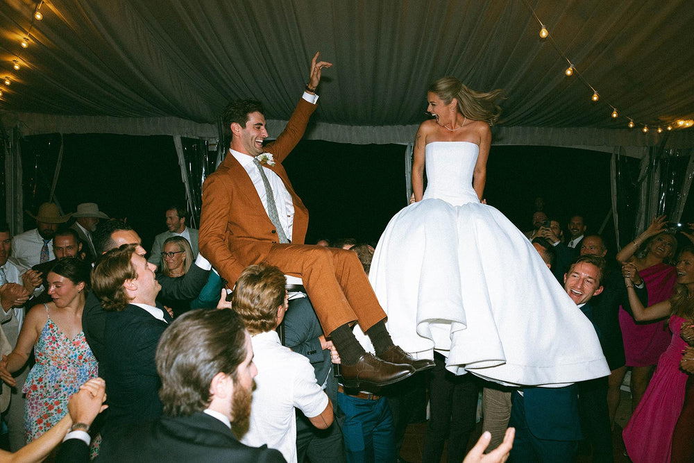 Joyful reception moment of Hannah and her groom dancing in a tent reception with warm string lights, Hannah in her custom strapless crepe wedding dress by Angela Kim Couture
