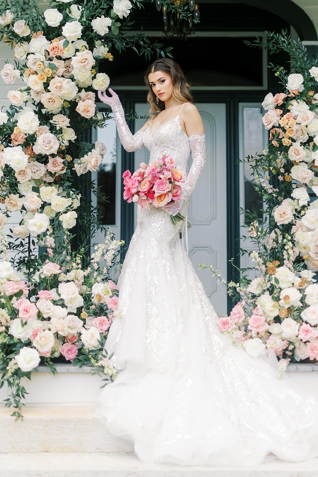 Kyra posing in her wedding gown with a bouquet among a beautiful flower arrangement.